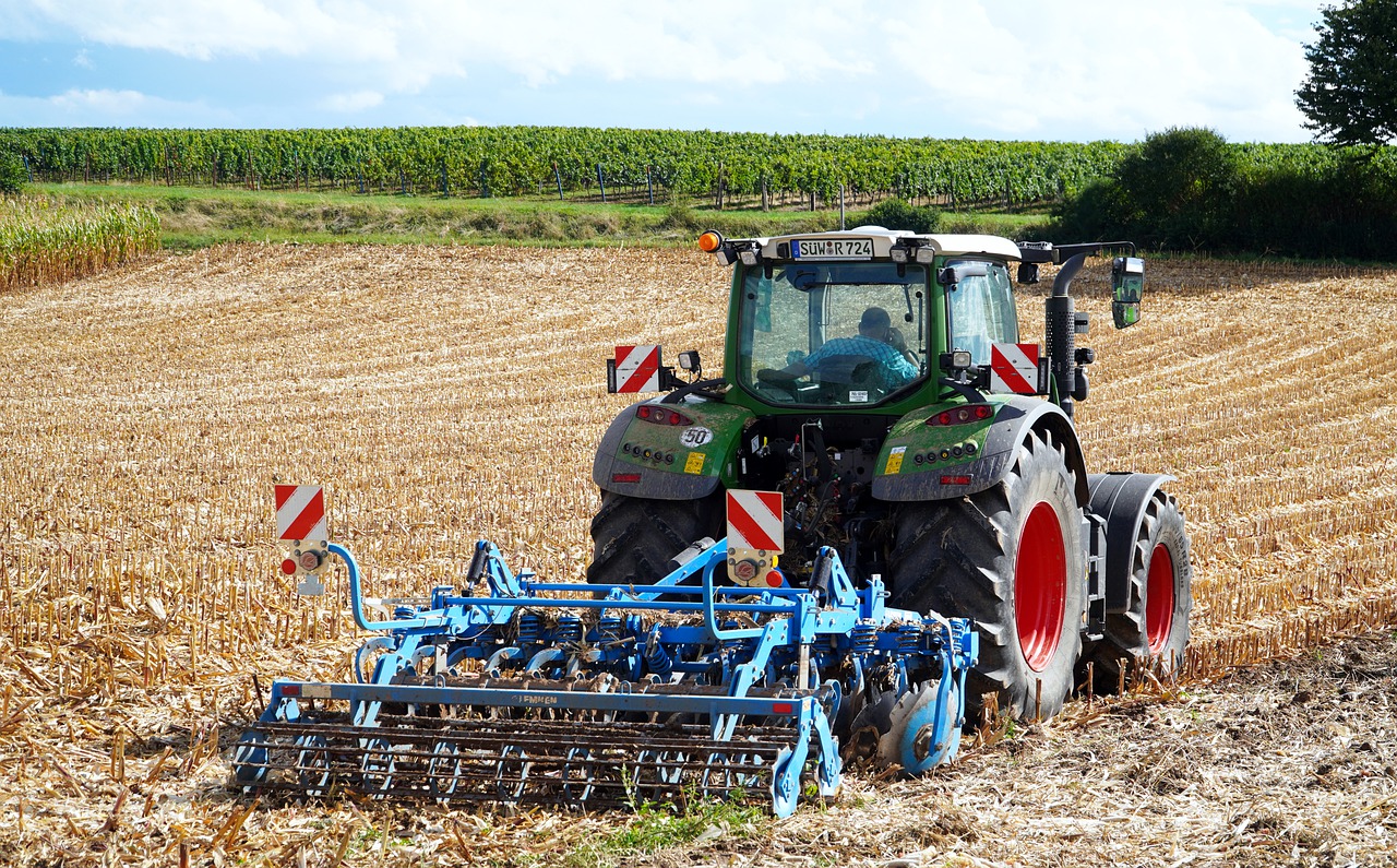Tracteur agricole rouge en action sur un champ verdoyant sous un ciel bleu